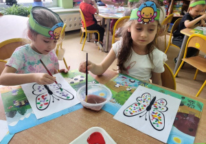 Dziewczynki malują motyle farbą.