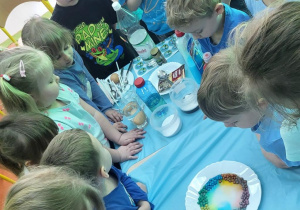 Dzieci obserwują zjawisko dyfuzji barwnika w wodzie.