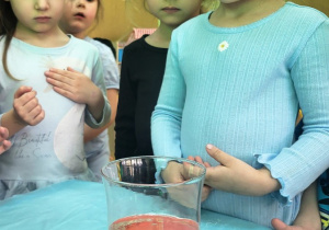 Przedszkolaki obserwują eksperyment z olejem i barwnikiem.