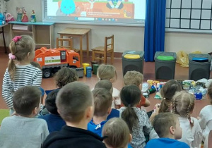 Dzieci oglądają film edukacyjny o segregacji śmieci.