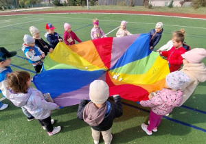 Dzieci bawią się chustą animacyjną i pomponami.