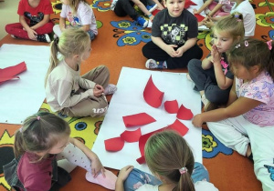 Motylki składają serce z kawałków czerwonego kartonu.