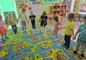 Dzieci przekazują sobie koło hula-hop bez użycia rąk.
