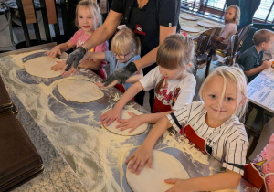Dziewczynki rozciągają ciasto na pizzę.