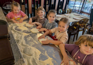Dziewczynki rozciągają ciasto na pizzę.