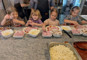 Dziewczynki układają dodatki na pizzy.