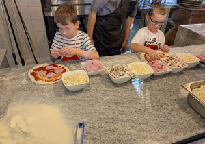 Chłopcy układają dodatki na pizzy.