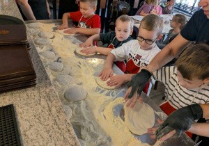Chłopcy rozciągają ciasto na pizzę.