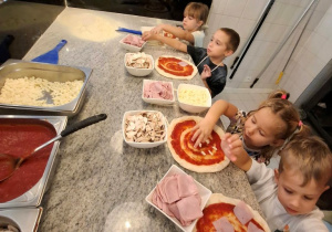 Dzieci układają składniki na pizzy.