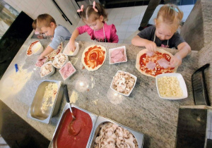 Dzieci układają składniki na pizzy.