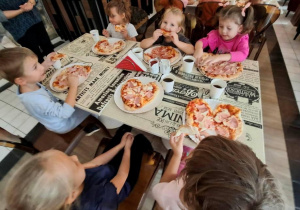 Dzieci degustują przygotowaną pizzę.