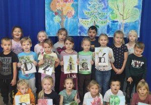 Motylki prezentują wykonane kredkami pastelowymi drzewa.
