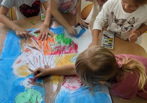 Dzieci kolorują kredkami pastelowymi drzewo jesienne.